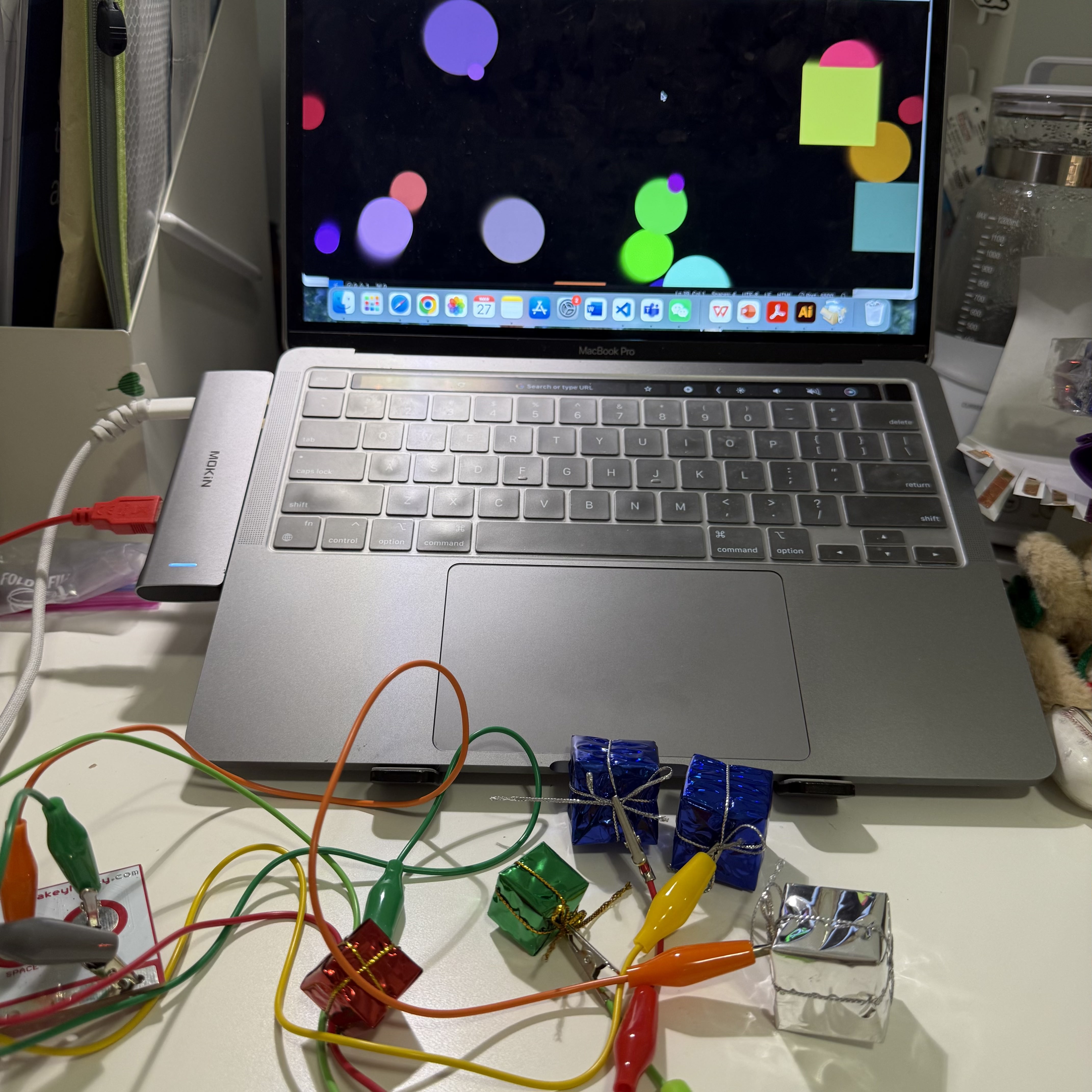In this setup, my laptop displays a colorful screen with floating bubbles. The gift-wrapped boxes connected to the Makey Makey board lie in front of the laptop. Each time I touch one of these boxes, it controls the movement or interaction on the screen, adding a playful element to my digital tasks.